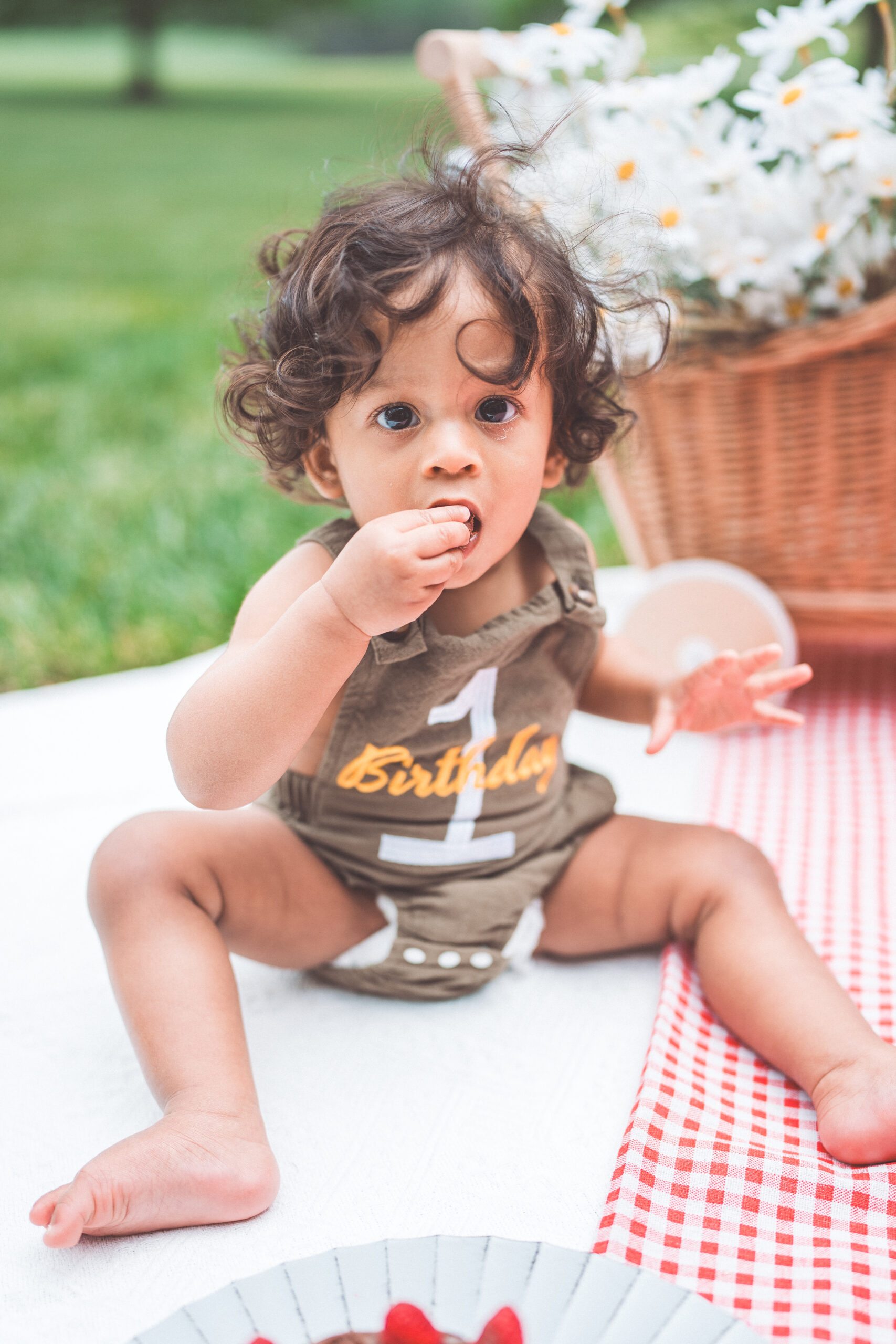 Toddler enjoying a chocolate cake smash while looking up at the camera beside a birthday cake.