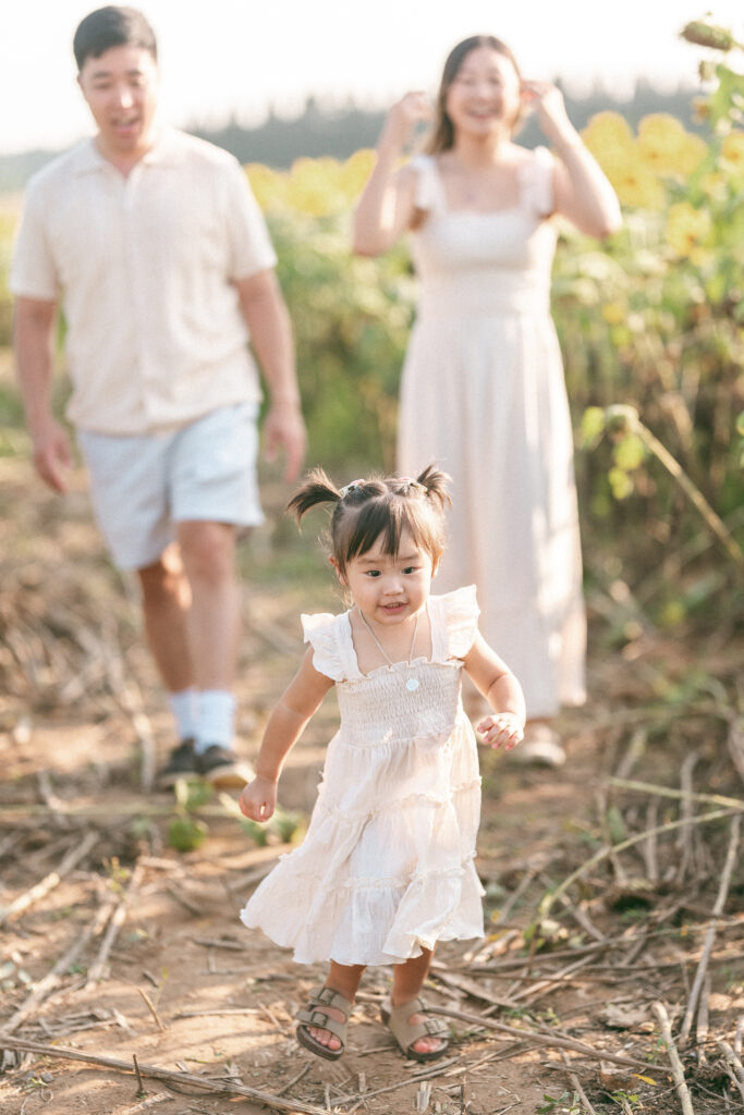 A child runs through sunflower fields with her parents close behind.