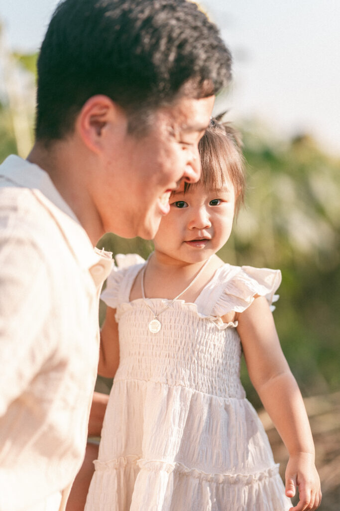 A toddler looks at the camera while standing next to her dad during their seasonal family sessions.