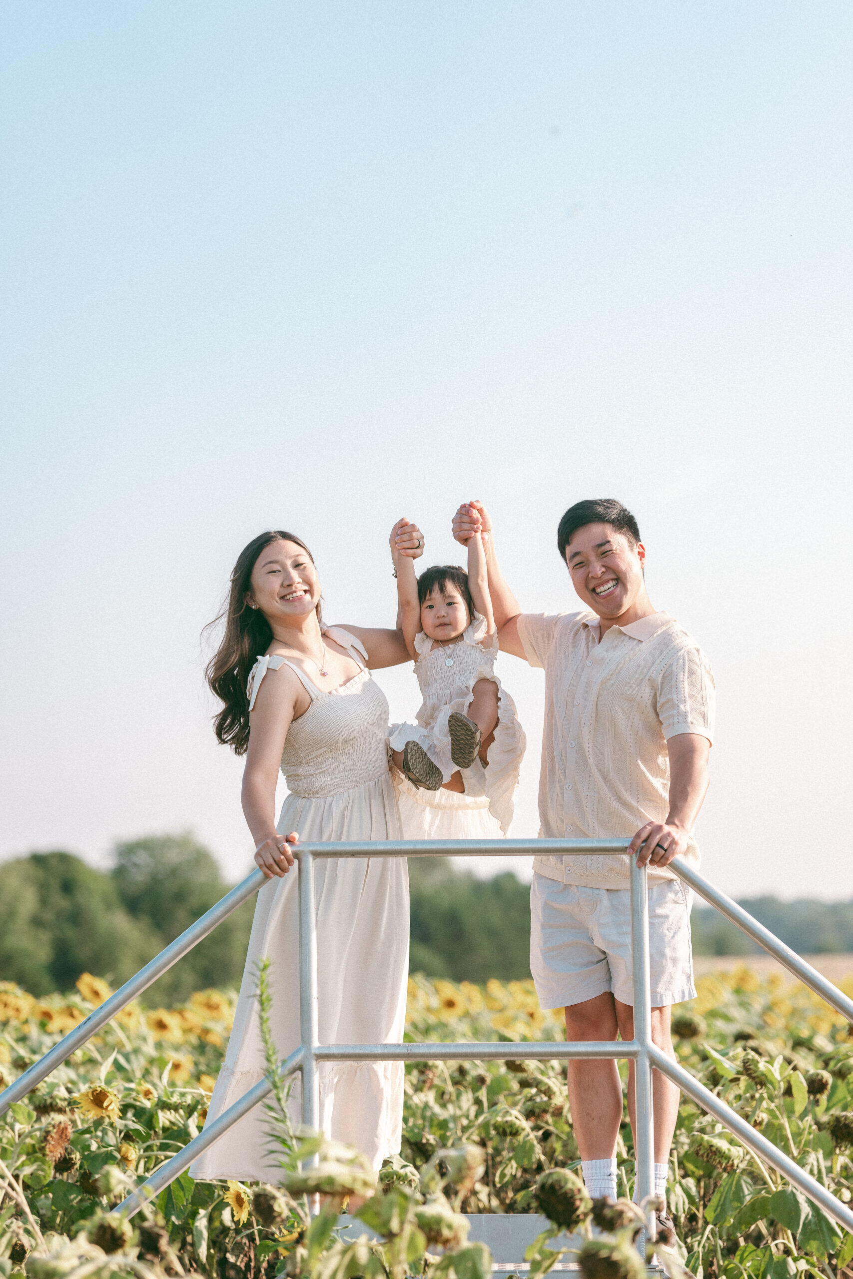 Family of three playing together on a farm platform overlooking a sunflower field.