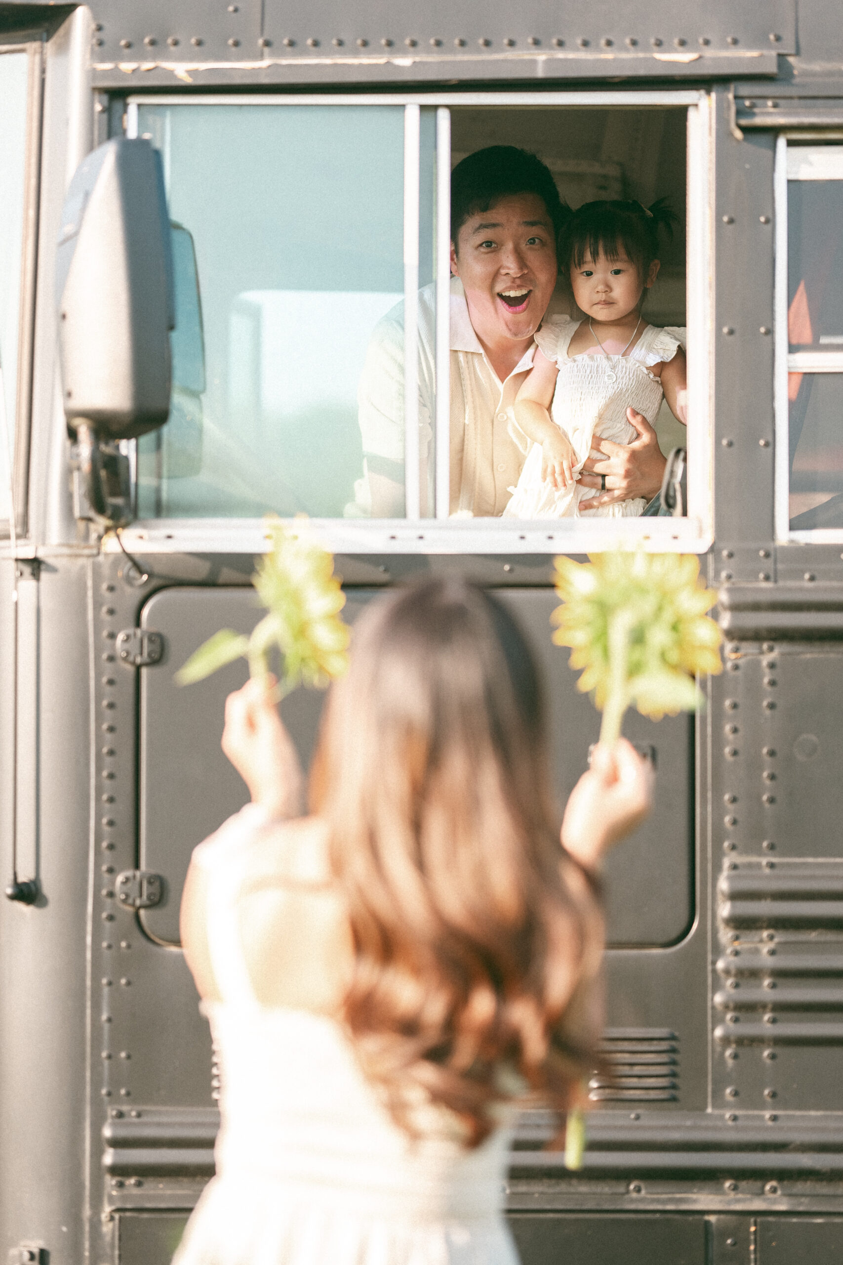 Mom showing dad and toddler sunflowers while standing outside of a bus.