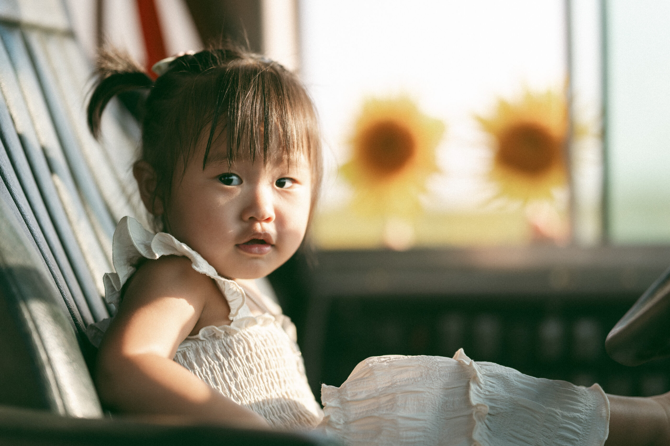 A toddler sits in the front drivers seat of a bus with sunflowers in the background.