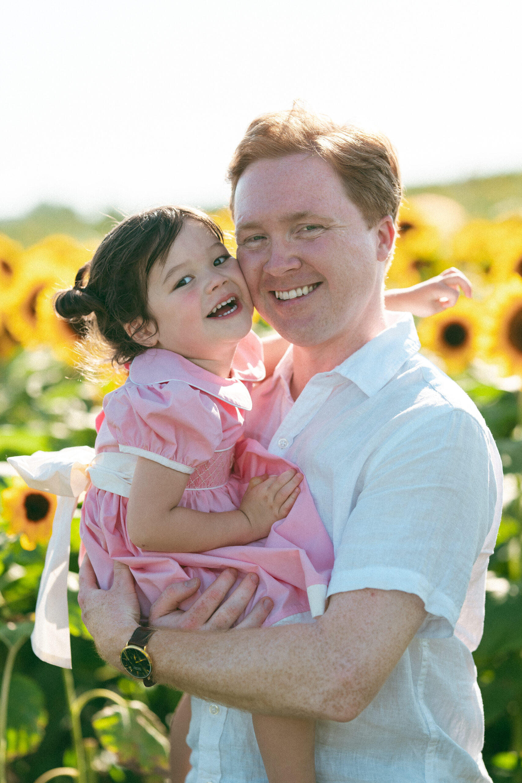 Dad holding his smiling young daughter in a pink dress during a summer family photoshoot.