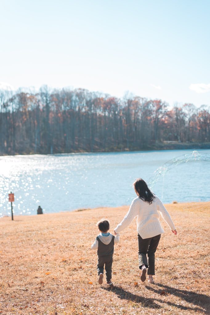 Mother and young son walking hand in hand toward the lake on a sunny autumn afternoon.
