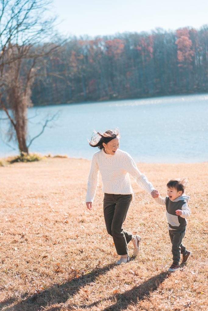 Mom running and laughing with her young son beside the lake on a sunny fall afternoon.