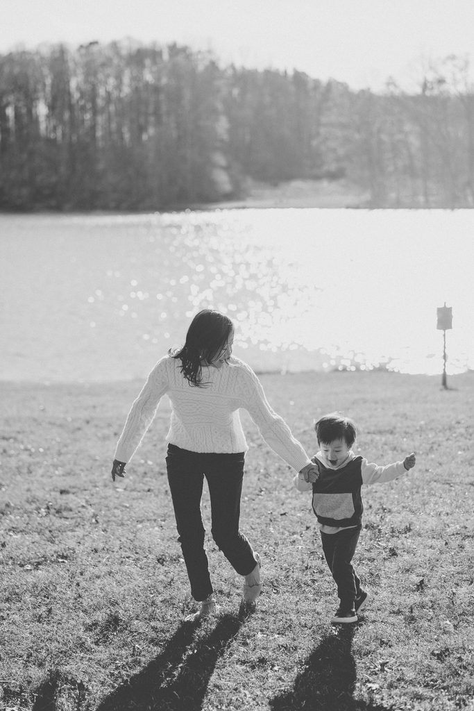 Black and white photo of a mother and young son running hand in hand during Seneca Creek State Park family photos.