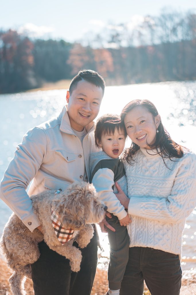 Family smiling together with their young son and dog during relaxed Seneca Creek State Park family photos by the water.