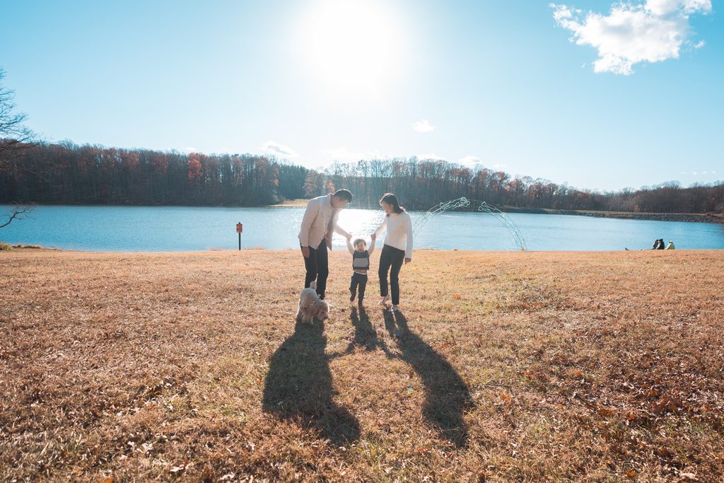 Parents walking with their young son and dog beside the lake on a bright fall afternoon.
