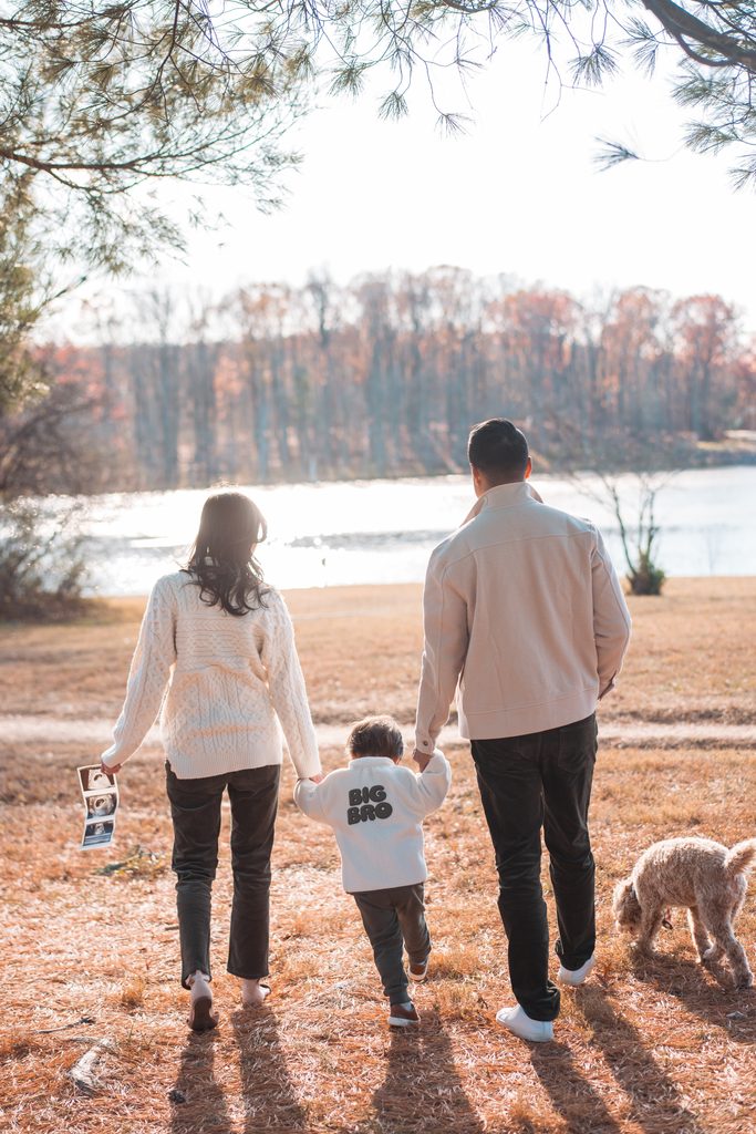 Mom and dad walking hand in hand with their toddler toward the lake during Seneca Creek State Park family photos.