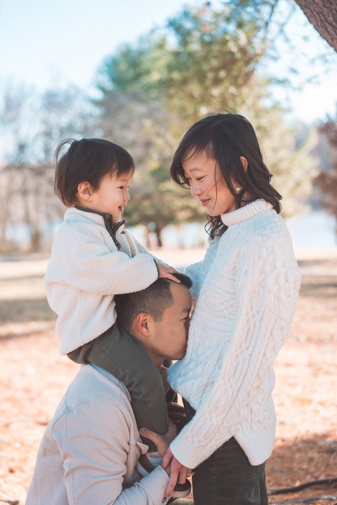 Dad kissing mom’s baby bump while their toddler sits on his shoulders during Seneca Creek State Park family photos.
