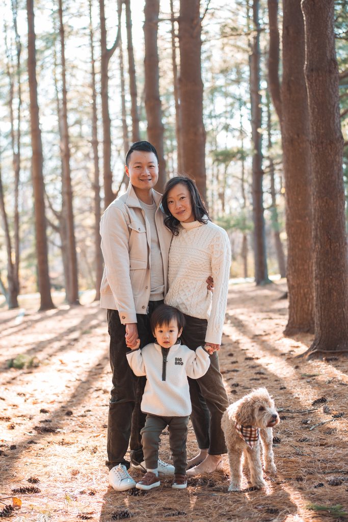 Family posing together among tall pine trees with their toddler and dog during Seneca Creek State Park family photos.
