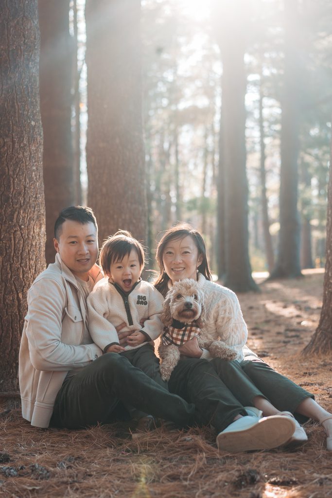 Family sitting together on the forest floor with their toddler and dog during Seneca Creek State Park family photos.