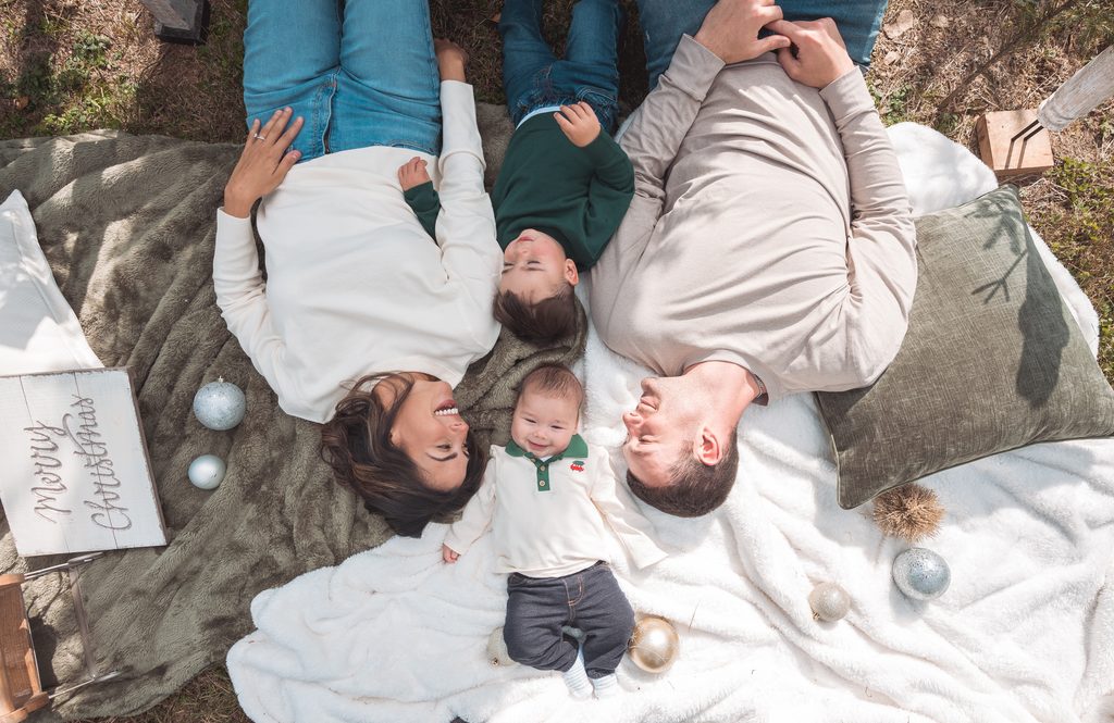 Family of four lying together on cozy blankets with Christmas ornaments during a playful holiday mini session.