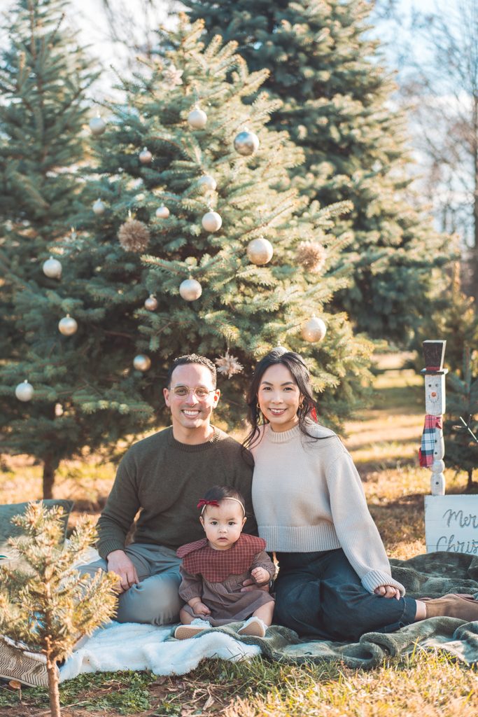 Family of three sitting together beneath a decorated Christmas tree during their festive holiday mini session.