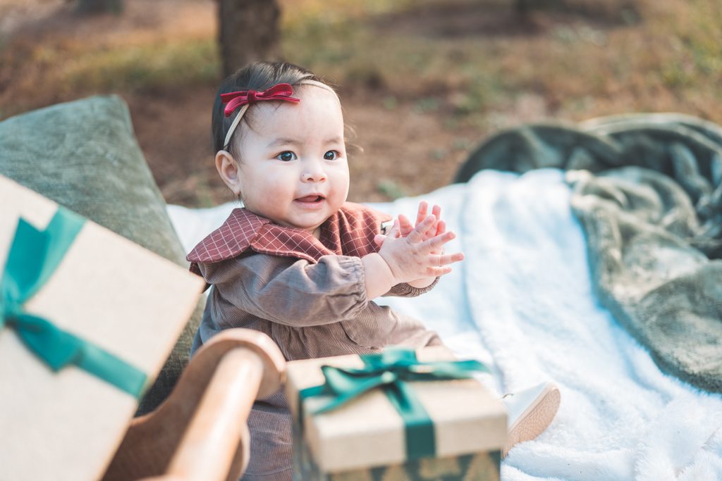 Baby girl wearing a red bow sitting beside a wrapped Christmas gift during a festive holiday mini session.